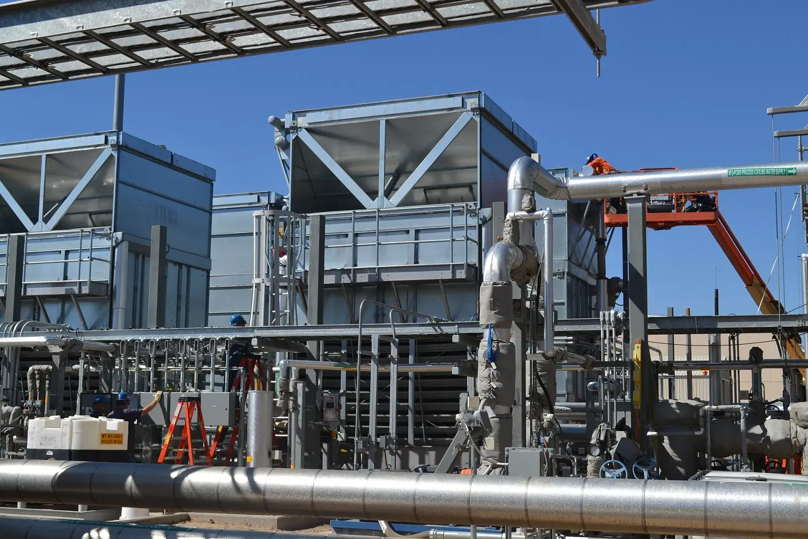 Industrial cooling installation with exposed pipework, cooling towers, and maintenance access platforms