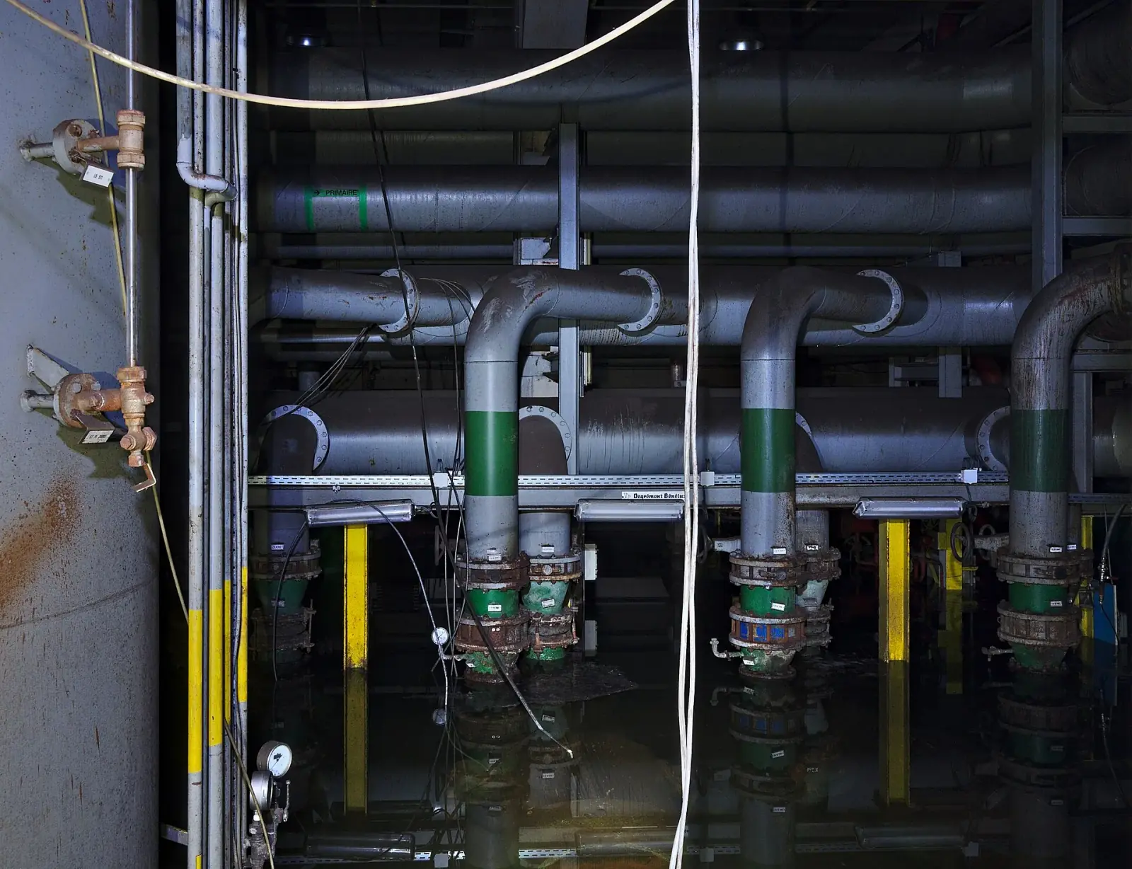 Flooded legacy pipe room with large exposed water-treatment pipes and valves