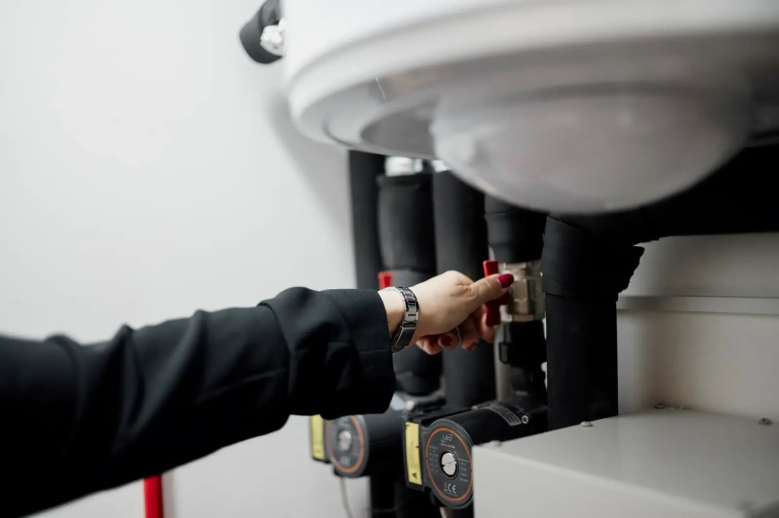 Operator turning a small red valve in a mechanical room with insulated pipework