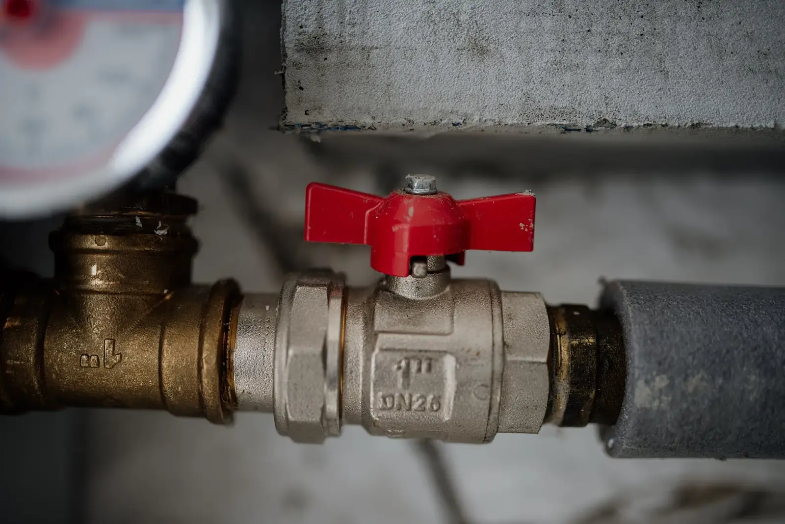Close-up of a red-handled metal valve and pressure gauge on exposed pipework
